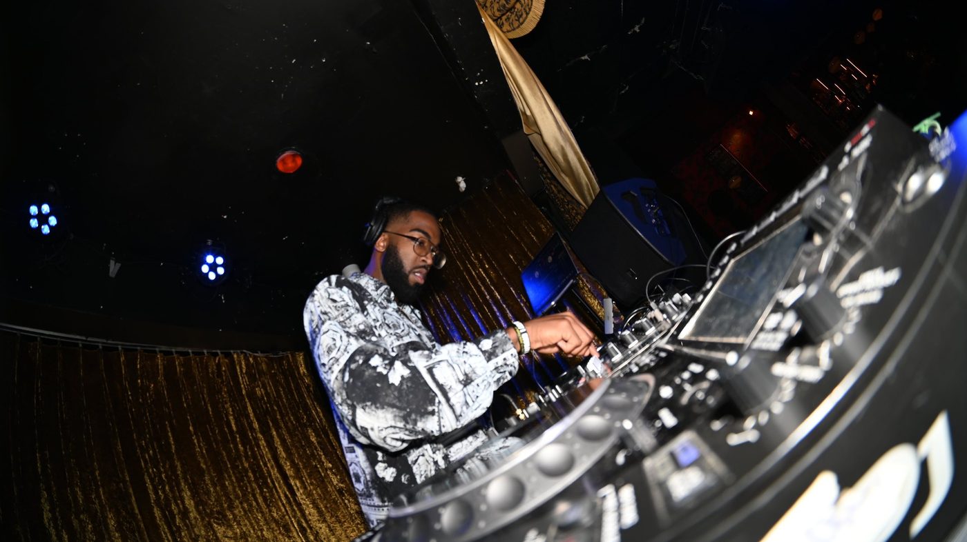 At the decks under club lights, a gold curtain behind